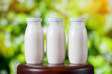 Natural liquid yogurt with probiotics in small plastic bottles on wooden table on background of green trees.