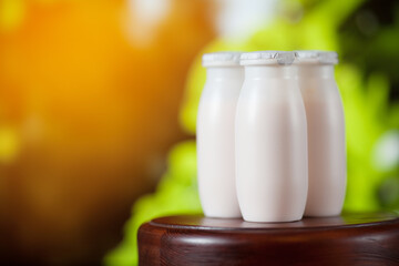 Natural liquid yogurt with probiotics in small plastic bottles on wooden table on background of green trees.