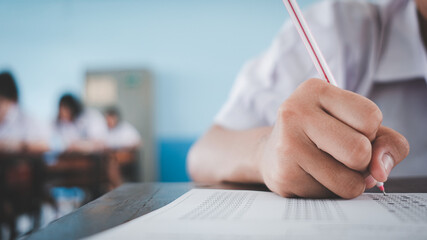Close up to students writing and reading exam answer sheets exercises in classroom of school with stress