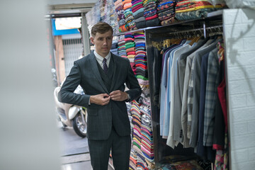 Handsome young businessman trying on new suit in atelier and looking at the mirror.