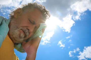 Senior man with towel suffering from heat stroke outdoors, low angle view. Space for text