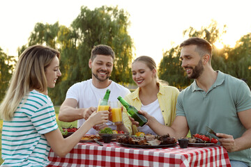 Happy friends with drinks and food at barbecue party in park