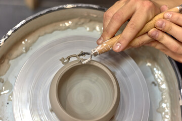 The hands of the master ceramist with a special tool align the almost finished cup on the potter's wheel