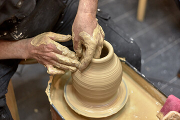 Hands of a ceramist in the process of making a large vase of light clay on a potter's wheel