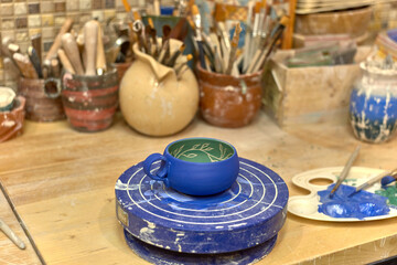 Painted blue and green cup made on a potter's wheel dries on a turntable for painting