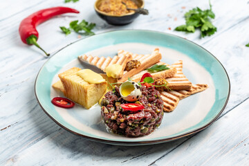 Tartare from beef with egg, capers, pickled cucumber with bread toasts served on plate. Healthy food trend