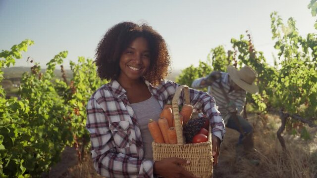 Mixed race female holding vegetable box smiling while male partner digs behind her