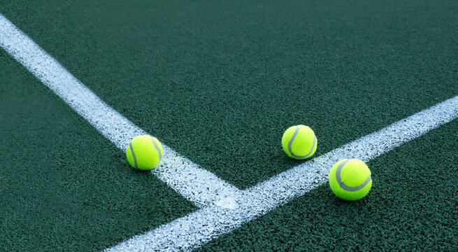 Three new tennis balls on the green tennis court,white lines.Empty space