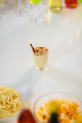 Tasty creamy spiced homemade eggnog drink with gingerbread in glass on middle of beverages table in Thanksgiving Christmas eve party surrounded by other alcoholic bottles liquor fries and snacks