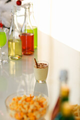 Tasty creamy spiced homemade eggnog drink with gingerbread in glass on middle of beverages table in Thanksgiving Christmas eve party surrounded by other alcoholic bottles liquor fries and snacks