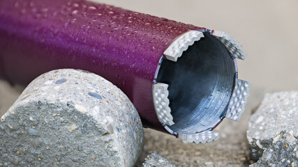Closeup of wet purple core drill bit and cylindrical bored piece of gray concrete tile. Drilling...