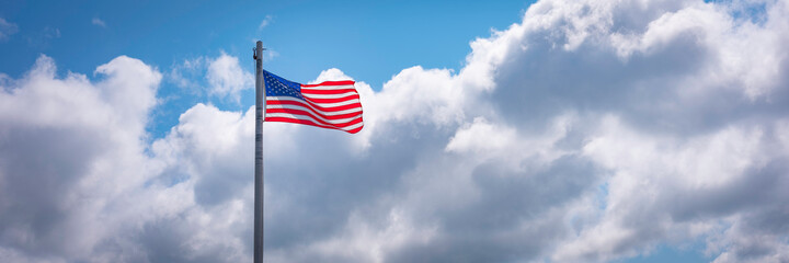 American Flag Waving in the Wind on White Clouds in the background. Blue Sky and Dramatic Clouds behind American Flag. Symbol of Unity and Leadership.