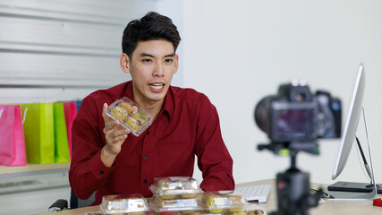Adult asian seller man look intend holding packaging of banana bread cupcake and looking at camera...