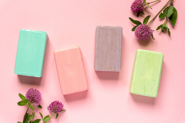 Flat lay of various natural soap bars with clover flowers on pink background, top view
