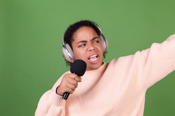 Beautiful african american woman on green background with wireless headphones and microphone...