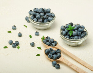 Fresh organic blueberries with leaves in  bowl and spoon  on grey background.  
