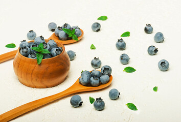Fresh organic blueberries with leaves in  bowl and spoon  on grey background.  