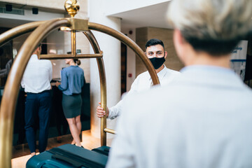 Bellboy helping guests with their luggage cart in hotel hallway. He takes guests' luggage to their rooms.