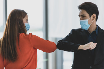 Young Asian businessman wearing protective hygiene mask and do elbow contact greeting with woman when meeting deal instead of shaking hands to prevent infection spreading of COVID-19 or coronavirus
