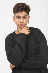 Fototapeta na wymiar Vertical front-view portrait shot of a handsome young boy teenager in black long sleeve clothes looking at the camera and posing hand to the chin gesture in the studio with a white background
