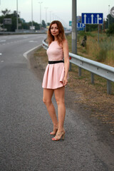 Fototapeta premium Alone beautiful woman in pink dress standing at the road