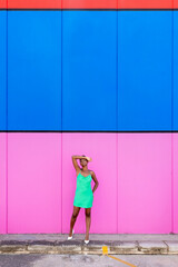 Stylish young black woman with electric green dress and white heels in front of a multicolored background