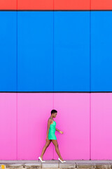 Stylish young black woman with electric green dress and white heels walking in front of a multicolored background