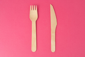 Wooden cutlery, disposable fork and knife isolated on pink background. Biodegradable wood table setting for food made from eco natural recycle reusable material.