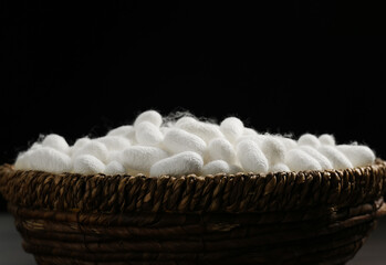 White silk cocoons in wicker bowl on black background, closeup