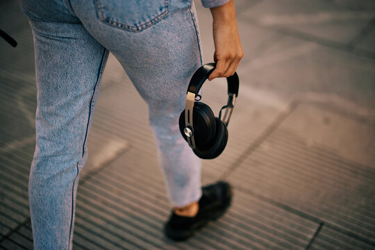Cut out picture of a young woman walking on the street and holding headphones in hand.
