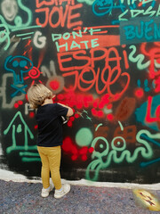 Caucasian three years old child painting graffiti on a wall at the street with a black t-shirt and yellow pants for the first time