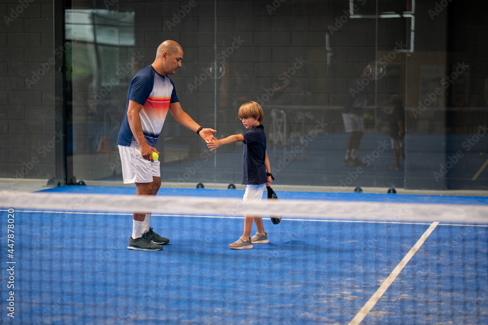 Wall mural monitor teaching padel class to child, his student - trainer teaches little boy how to play padel on