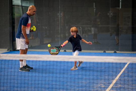 Monitor teaching padel class to child, his student - Trainer teaches little boy how to play padel on indoor tennis court