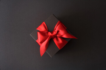 Black gift box with red bow on black background