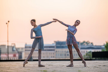 Fototapeta premium Two young ballerinas dancing in pointe shoes in city against the backdrop of sunset sky