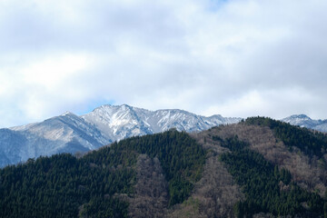 Beautiful snow mountain view with green forest and dry trees on blue clouds sky in morning time,the view from shirakawago village,Japan.
