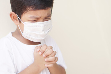 Little Asian boy praying and worship to GOD for stop spirituality and Surrender concept. Cover the mask to protect the germ or virus from the air. 2019-Corona virus or Covid-19.