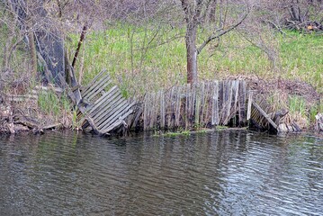 Naklejka premium part of a broken old gray wooden fence on the shore and in the water of the lake