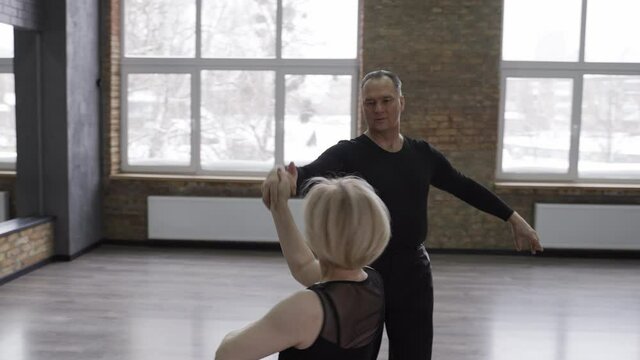 Close-up of spectacular ball dancing couple during training, man whirling attractive disabled woman sitting on wheelchair. Beautiful blonde female with impaired mobility and her partner during dance