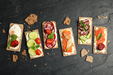 Fresh rye crispbreads with different toppings on black table, flat lay
