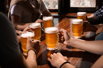 Friends with tasty beer at wooden table in pub, closeup