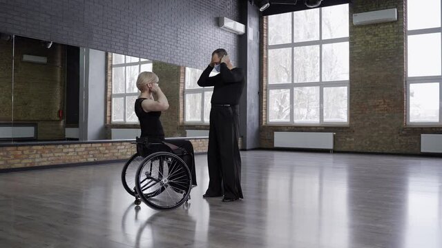 Professional ball dancing couple, mature man and woman on wheelchair wearing medical masks before training in dance hall during coronavirus epidemic. Handicapped female and her partner before dance