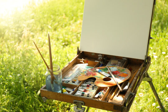 Easel with blank canvas and painting equipment in countryside