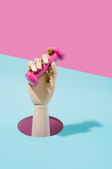 Wooden hand with a pink dumbbell on blue and pink background. Sport and exercise. 3d illustration