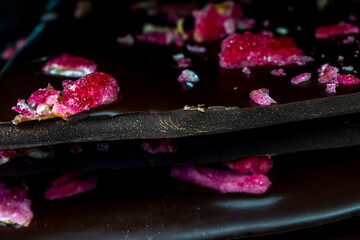 Selective focus. Black chocolate tile with red dried and fresh berries and candied flower leaves....