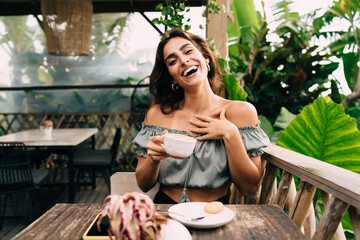 Cheerful woman drinking cappuccino at cafe table on summer terrace