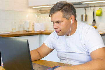 Fototapeta premium smiling European man working on laptop in his kitchen. home Office. businessman at home