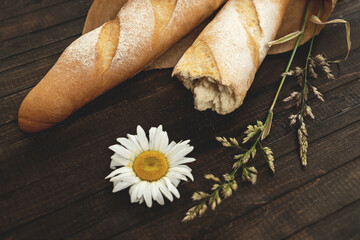 Golden wheat baguettes. Two craft loaves of crispy bread on brown wooden table with wildflowers on it. Top view. Horizontal format.