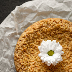 Romantic dessert. Cake or shortcrust pastry tart decorated with white gerbera flower on parchment paper. Close-up shot. Top view.