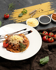 Italian lunch. Plate of noodles with tomato sauce, tomatoes and grated Parmesan cheese on table with ingredients on it. Vertical format.